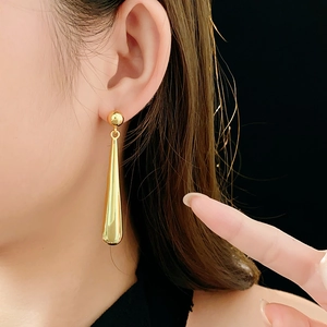 Close-up of model wearing gold long teardrop earrings with a polished metallic finish