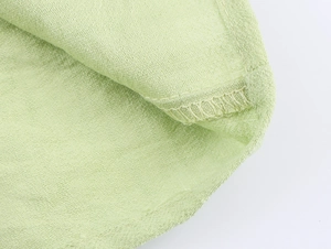 Close-up of light green textured fabric with fine stitching details and lantern sleeve edge