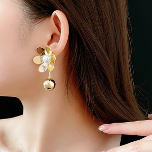 Détail de boucles d'oreilles fleur avec perle blanche et boule dorée sur un mannequin