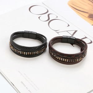 Detail of layered braided leather bracelets in black and dark brown with metal rivets