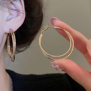 Detail of double-layer intertwined gold hoop earrings with matte and polished finishes