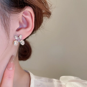 Close-up of silver bow-shaped earrings with large sparkling zircon stones on model
