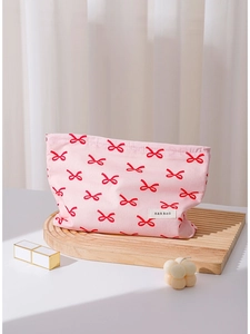 Pink cotton makeup bag with red bow pattern on wooden tray with beauty accessories