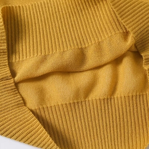 Detailed close-up of the ginger yellow knitted fabric texture and ribbed hem craftsmanship