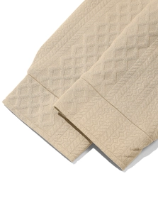 Macro shot of knitted beige shirt cuff showing detailed jacquard texture and premium fabric