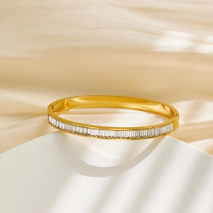 Close-up of gold stainless steel bangle with square-cut crystal on silk background