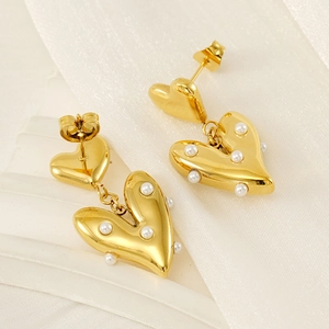 Elegant gold heart earrings with pearl inlay on white fabric, minimalist fashion jewelry