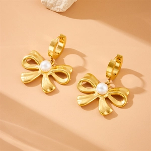 Gold plated vintage woven chain earrings with bow tie design and pearls on beige surface