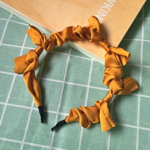 Close-up of a yellow pleated fabric headband on a green grid background surface