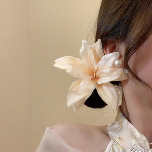 Detailed view of champagne fabric lily hair clip with a pearl center on a female model