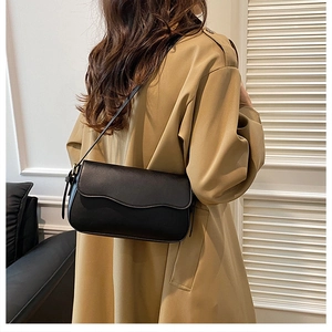 Close-up of minimalist black leather crossbody bag with wavy flap edge on trench coat