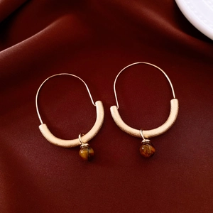Detailed close-up of golden hoop earrings with tiger eye beads on red silk background