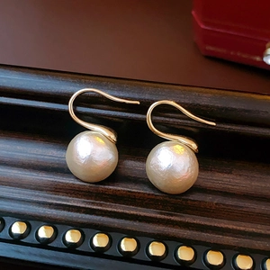 Détail de boucles d'oreilles crochet dorées avec de grandes perles rondes brillantes