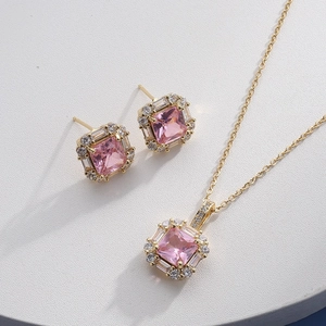 Close-up of golden necklace and earrings set with pink square stones and small diamonds