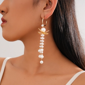Detailed view of long gold tassel earrings with leaf design and white faux pearls on model