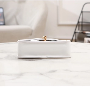 Close-up of white quilted leather crossbody bag with golden chain tassel on marble surface