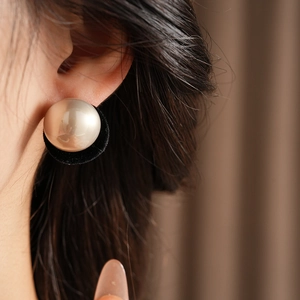 Close-up of pearl earrings with black velvet base worn by model on soft background