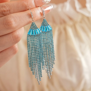 Close-up of bohemian fan-shaped tassel earrings with turquoise zircons and silver plating