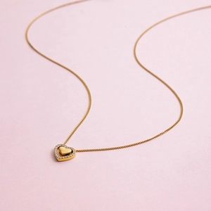 Macro detail of 18K gold stainless steel necklace with sparkling heart pendant on pink