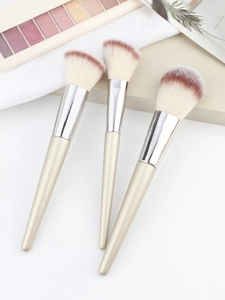 Close-up of three champagne makeup brushes with gradient bristles on aesthetic background