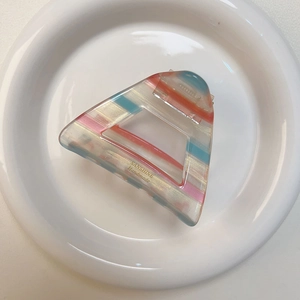 Molla per capelli triangolare a righe in acetato con logo dorato su piatto bianco