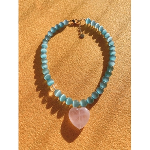 Blue cat eye bead necklace with a pink crystal heart pendant on orange background