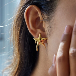 Polished gold-tone stainless steel liquid star stud earrings worn by a female model