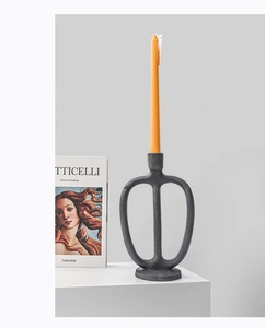 Detail of a matte black abstract candle holder with an orange taper candle on a pedestal