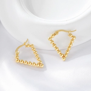 Macro detail of gold plated beaded triangle earrings on white silk and geometric tray