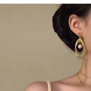 Detail view of multi-layer hollow golden teardrop earrings with a white pearl on a model
