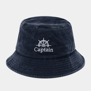 Close-up of white Captain embroidery and ship wheel logo on navy blue washed bucket hat