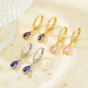 Detailed macro view of gold and silver huggie earrings with pear-cut zircon pendants