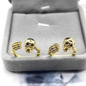 Close-up of golden skull rings with adjustable open bands inside a grey velvet jewelry box