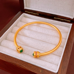 Détail d'un bracelet plaqué or 18k avec fini mat et pierres précieuses rouge et vert