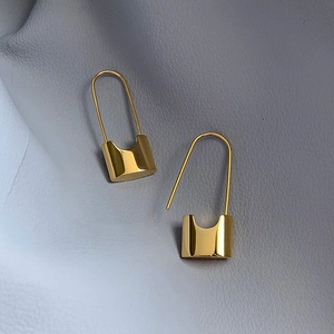 Detailed macro view of minimalist golden pin lock earrings on blue leather surface