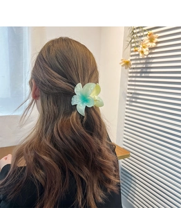 Green and yellow gradient frangipani flower hair claw clip worn on wavy brown hair