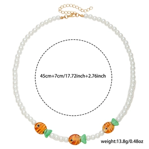 Close-up of pearl necklace with orange and green fish charms and gold clasp details