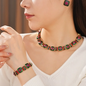 Close-up of vintage gold necklace and earrings set with green enamel and red gems