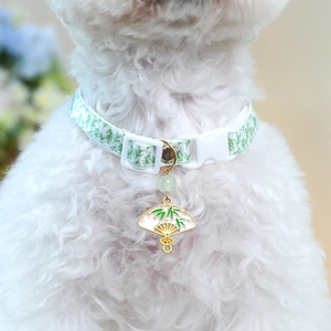 Close-up of green bamboo pattern pet collar with a gold-edged fan charm on a white dog
