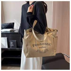 Detail of a large beige canvas tote bag with black typography and side pocket on shoulder