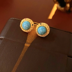 Macro shot of 18k gold plated turquoise stud earrings with vintage texture on leather