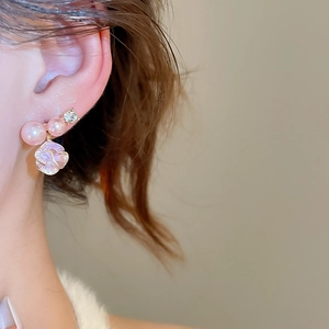 Dettaglio di orecchini a fiore con perle rosa e strass scintillanti sul modello