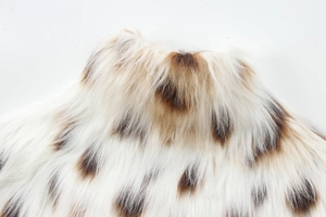 Macro shot of faux fur jacket fabric with brown spots on a soft pearl white surface