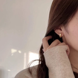 Close-up of minimalist chunky gold hoop earring worn by a model in beige knitwear