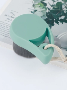 Detailed macro of a green facial brush featuring dense grey bristles and a cotton lanyard