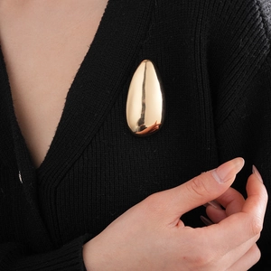 Macro view of a large golden teardrop brooch styled on a minimalist black knit garment