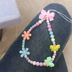 Close-up of colorful beaded phone strap with acrylic bow and flower charms on denim