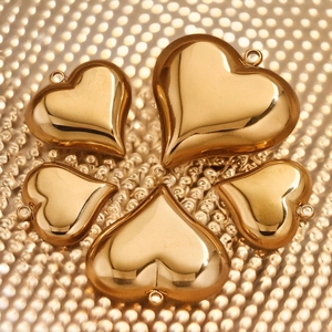 Five sizes of polished gold stainless steel heart charms on reflective background
