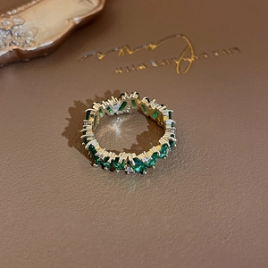 Detailed close-up of gold plated ring with emerald green and zircon stones on leather background