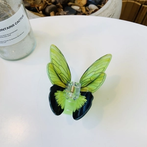 Elegant green acrylic butterfly hair claw clip with golden spring on a white surface